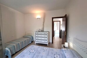 A bedroom with two single beds, a white dresser, a bedside table with a lamp, and a door leading to another room. - Casa Luisa in Capoliveri (Capoliveri)