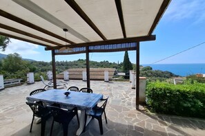 An outdoor patio with a table and chairs, a pergola, stone flooring, and a scenic view of the sea and hills. - Casa Luisa in Capoliveri (Capoliveri)