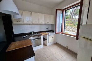 A compact kitchen with white cabinets, a stove, oven, and a window with a view of trees. - Casa Luisa in Capoliveri (Capoliveri)