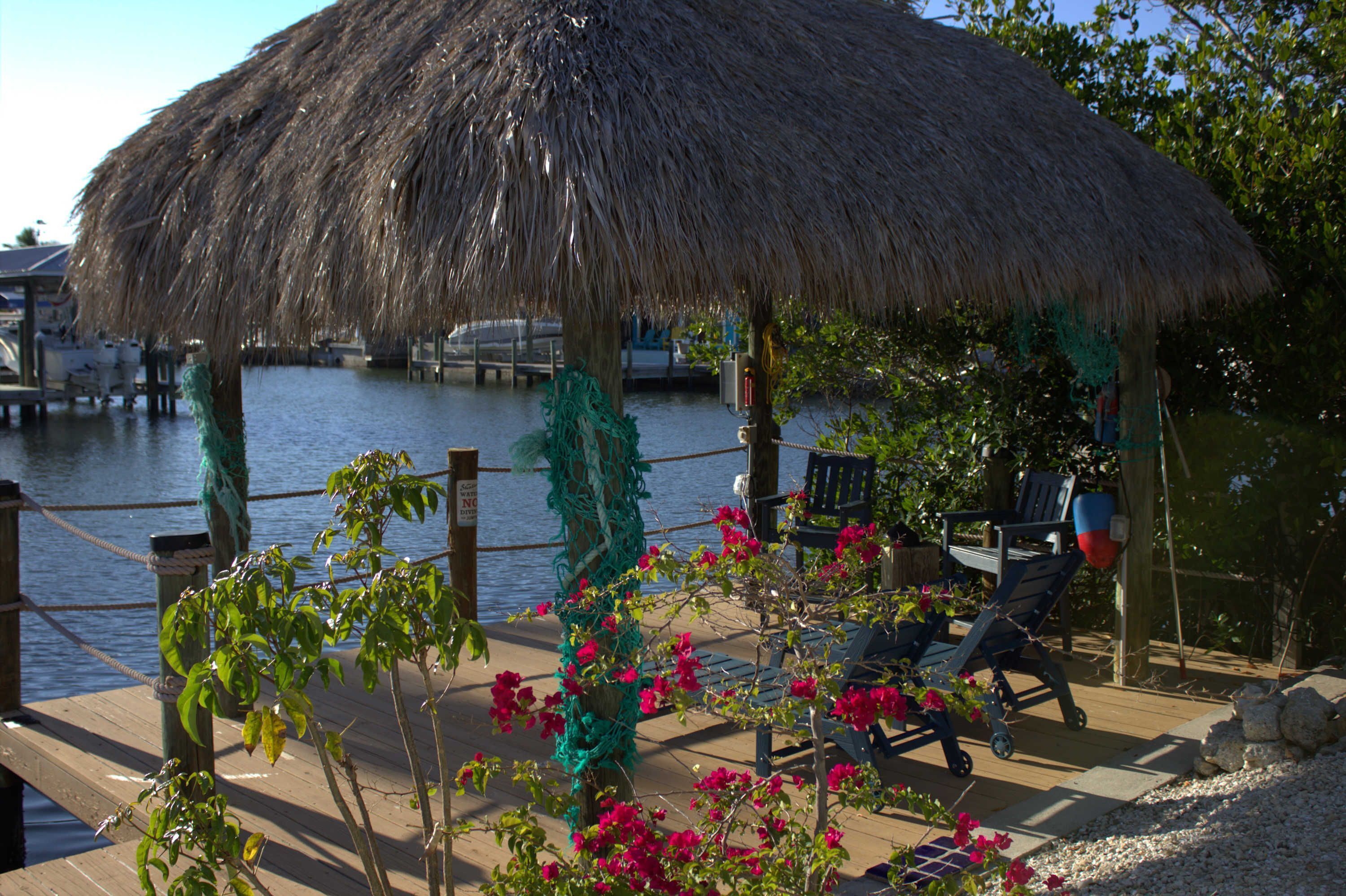 A thatched-roof structure with a view of water, a dock, and a chair by the railing.
