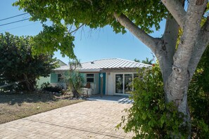 A house with a tiled driveway, a front porch, and a tree in the foreground. - Island Style Waterfront Retreat w Private Dock (Saint James City)