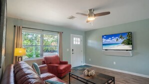 Un salon comprenant un canapé, un fauteuil, une table basse, un téléviseur, un ventilateur de plafond et une vue sur la verdure à l’extérieur.