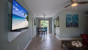 Un salon moderne doté d’un grand téléviseur à écran plat, d’un coin repas, d’un ventilateur de plafond et d’œuvres d’art accrochées aux murs.