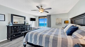 Een slaapkamer met een bed, een plafondventilator, een televisie, een dressoir en uitzicht op de oceaan.