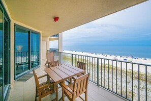 Ein Balkon mit Tisch und Stühlen mit Blick auf einen Strand mit Sonnenschirmen.