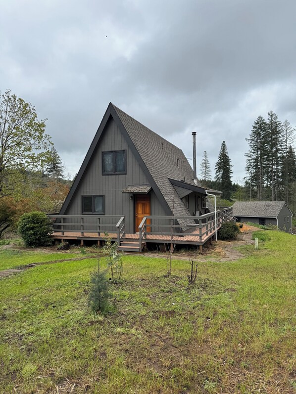 A modern, gray, triangular-roofed house with a wooden deck and a chimney.