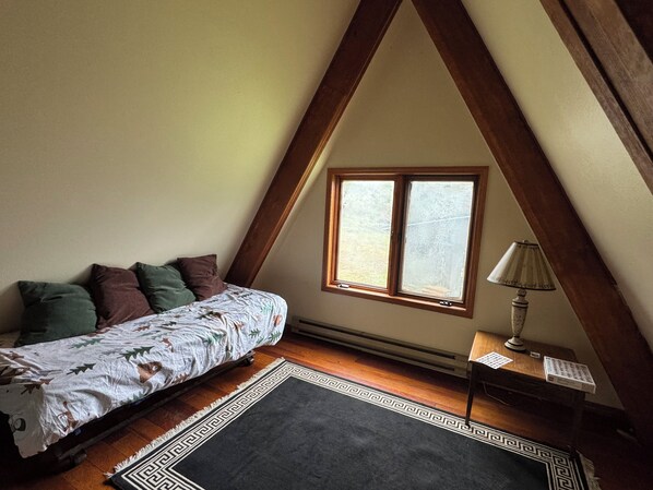 Un dormitorio con techo inclinado, cama con ropa de cama estampada, una ventana, una lámpara y una alfombra.