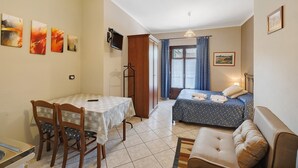 A room with a bed, a table with chairs, a sofa, and artwork on the walls. - Studio 'Luna' with Shared Garden, Balcony and Wi-Fi (Monforte d'Alba)