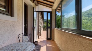 A balcony with a table and chairs, a view of a mountainous landscape, and a door leading outside.