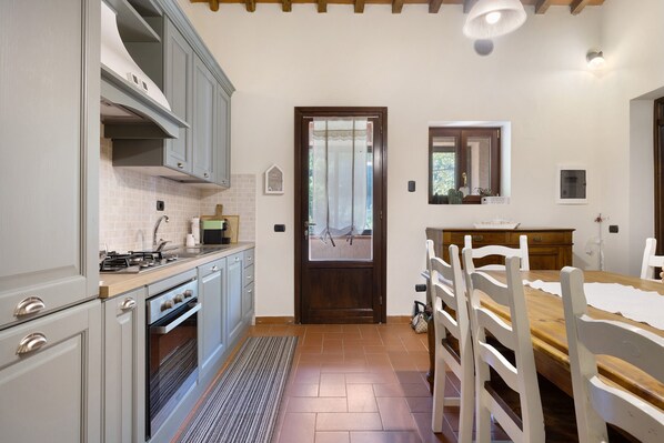 A kitchen with modern appliances, a dining area with a wooden table and chairs, and a door leading to a balcony.