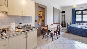 Een keuken met een spoelbak, fornuis en kasten, een eettafel met stoelen, en een bed met een blauwe spreidekker.