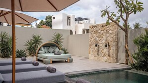 Un espace aménagé au bord de la piscine, comprenant une chaise longue, un petit coin salon et un mur en pierre.