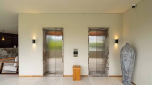 Un hall d’entrée moderne avec deux ascenseurs, un comptoir de réception, une petite table d’appoint en bois et un grand vase.