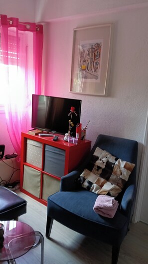 A living room with a TV, a red cabinet, a blue armchair, and a framed picture on the wall. - Room-lisbon Nice & Cousy Room (Lisbon)