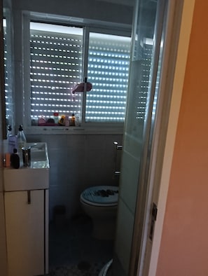 A small bathroom with a toilet, a sink, and a window with blinds. - Room-lisbon Nice & Cousy Room (Lisbon)