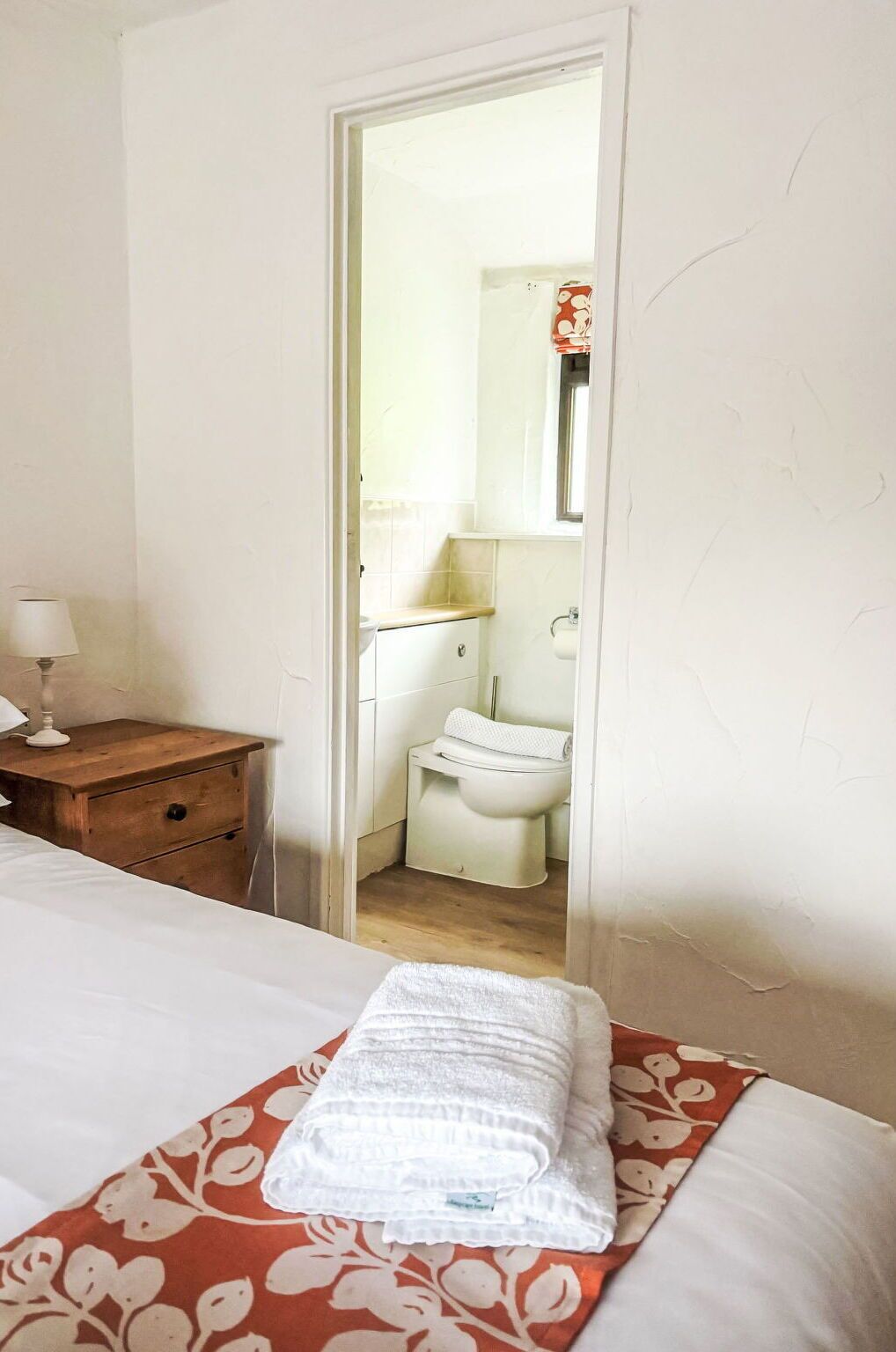 A bedroom with a bed, a nightstand, a bathroom visible through an open door, and a towel on the bed.