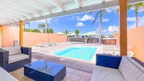 Un espace extérieur abrité comprenant une piscine, des chaises longues et un canapé.