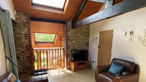 Ett mysigt vardagsrum med en öppen spis, lädersoffor, en tv och en balkong med ett träräcke.