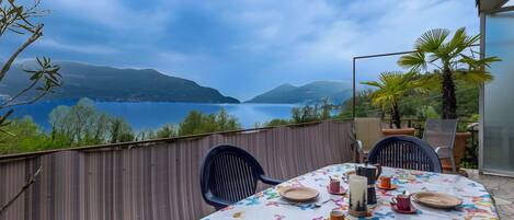 An outdoor dining area with a table set for two, overlooking a body of water and hills.