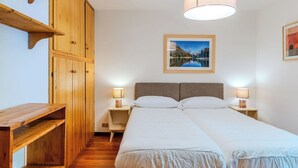 Et soveværelse med et træskab, en seng med to puder, et sengebord med en lampe og et billede i ramme på væggen.