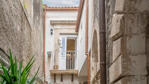Un vicolo stretto con un edificio bianco, un balcone con ringhiera in metallo e una porta con una finestra.