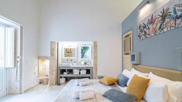 Una camera da letto con un letto, un bagno con un lavandino e uno specchio, e un muro decorato con un murales di piante.