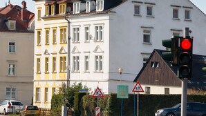 Rua com um edifício branco, um semáforo vermelho e placa de faixa de pedestres.