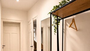 Um corredor com piso de madeira, porta branca e um espelho com uma planta em cima.