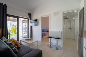 Ein modernes Wohnzimmer mit einer Couch, einem Fernseher, einem kleinen Tisch und einer Glastür, die auf einen Balkon führt.