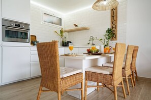 A modern kitchen with white cabinetry, a built-in oven, wicker chairs, and a hanging light fixture. - Royal Blue San Agustin (San Bartolomé de Tirajana)