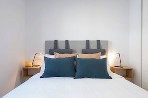 Ein ordentlich bezogenes Bett mit Kopfteil, zwei Nachttische mit Lampen und einem an der Wand befestigten Regal.