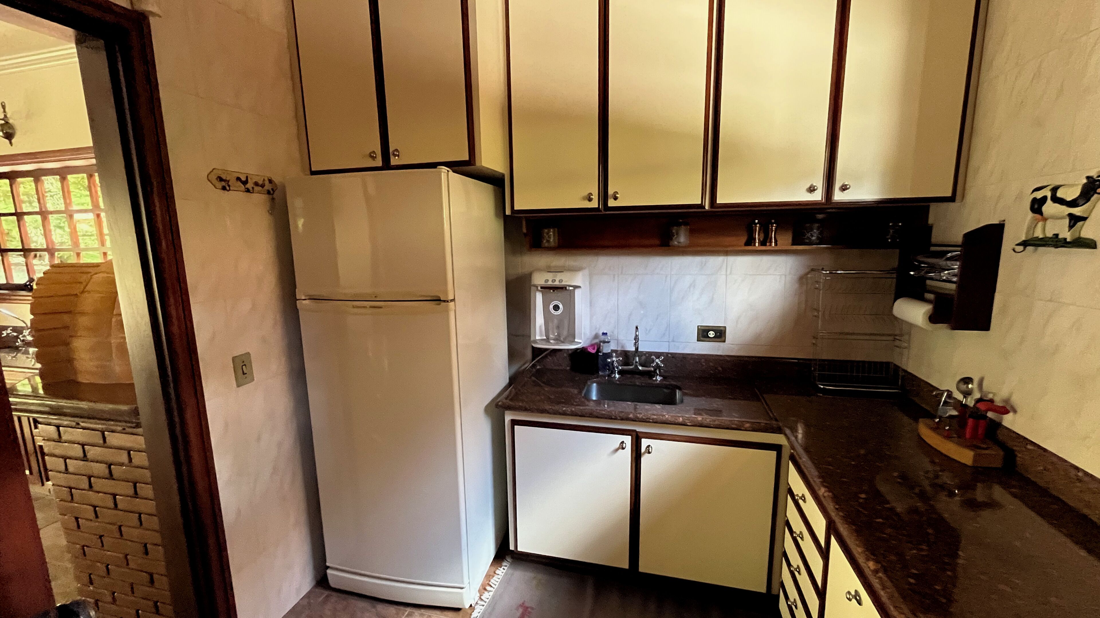 A compact kitchen with white cabinets, a refrigerator, a coffee maker, and a sink.