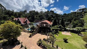 A two-story house with a red-tiled roof, a swimming pool, and a well-maintained garden with various plants and a lawn. - Casa Jardim Véu da Noiva (Campos do Jordão)