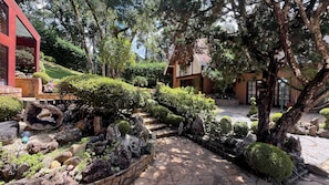 A garden with stone pathways, neatly trimmed bushes, and a red building. - Casa Jardim Véu da Noiva (Campos do Jordão)