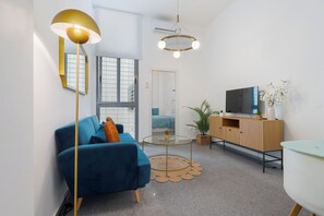 A modern living room with a blue sofa, a round glass coffee table, a TV on a wooden cabinet, and a pendant light. - Charming Sevillian corner in the historic center of Seville (Sevilla)