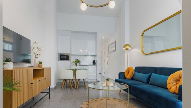 Un salon moderne avec un canapé bleu, un téléviseur, un coin repas et une cuisine.