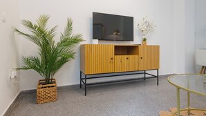 Un salon moderne avec un meuble en bois, un téléviseur à écran plat, une table en verre et une plante en pot.