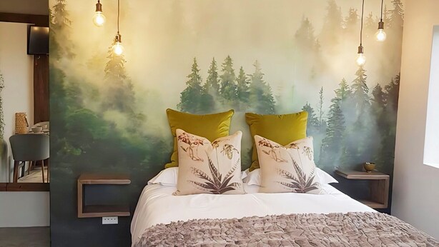 A bedroom with a bed, a wall mural, a ceiling light fixture, and bedside tables. - Charming Garden Route Villa, Nature View and BBQ Bliss (Mossel Bay)