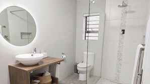 A modern bathroom with a round mirror, a sink, a toilet, and a shower area. - Charming Garden Route Villa, Nature View and BBQ Bliss (Mossel Bay)