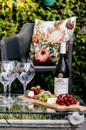 Une table en verre avec une bouteille de vin, des verres et une planche de fromages accompagnée de raisins et de noix.