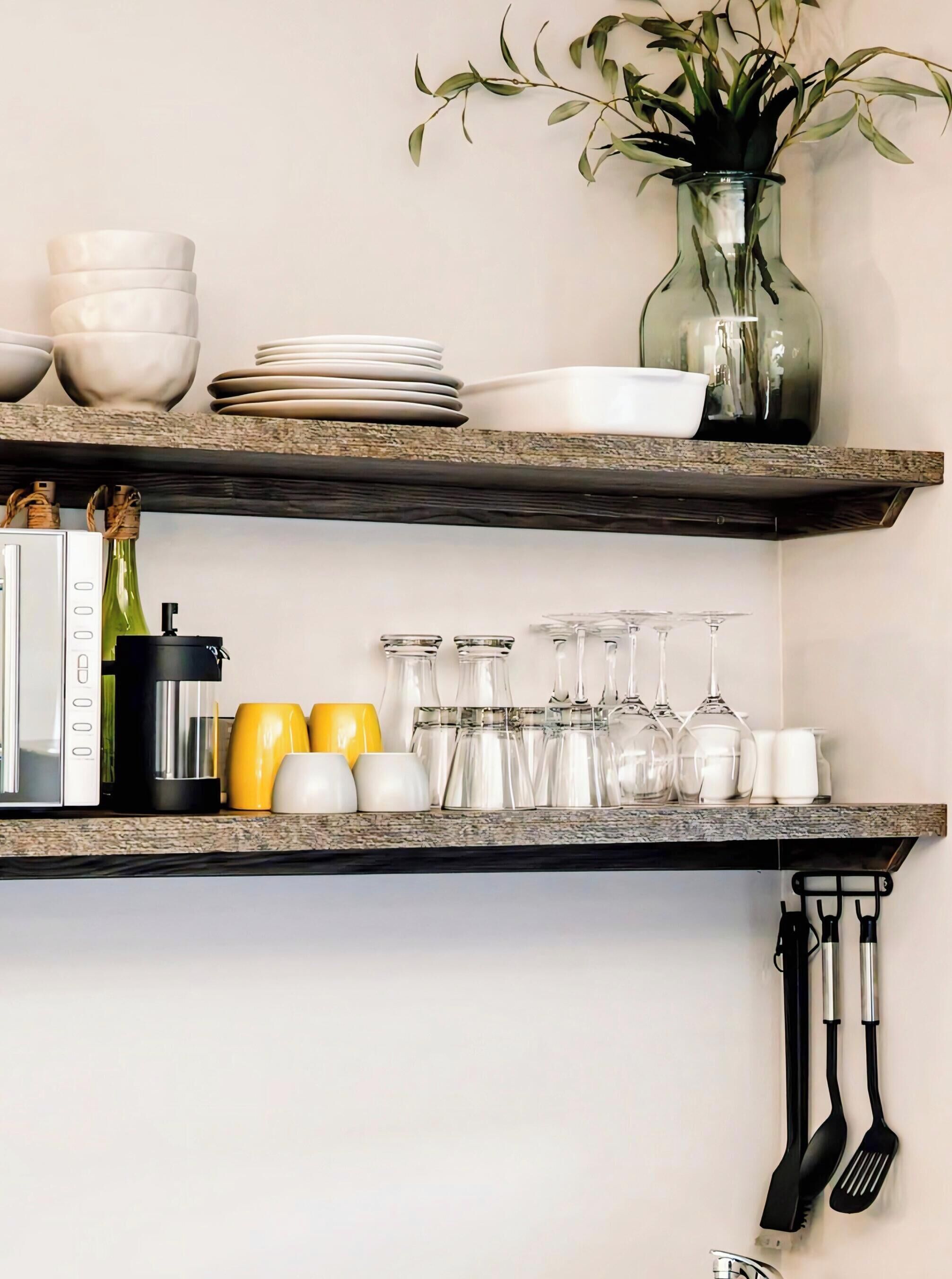 Une étagère de cuisine avec des assiettes blanches, un vase avec des feuilles vertes, une machine à café et de la verrerie.