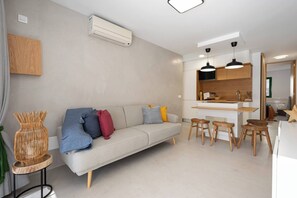 Una sala de estar moderna con un sofá, un comedor con taburetes y una cocina con armarios de madera.