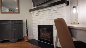 Un salón con chimenea, un televisor montado encima y un mueble de color oscuro.