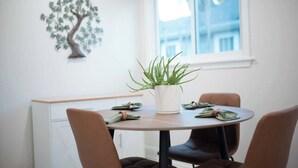 Un área de comedor con una mesa redonda, cuatro sillas, una planta en maceta y un adorno de árbol en la pared.