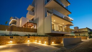 Un immeuble moderne à plusieurs étages, doté de balcons, d’un mur de soutènement en pierre et d’un éclairage extérieur décoratif.