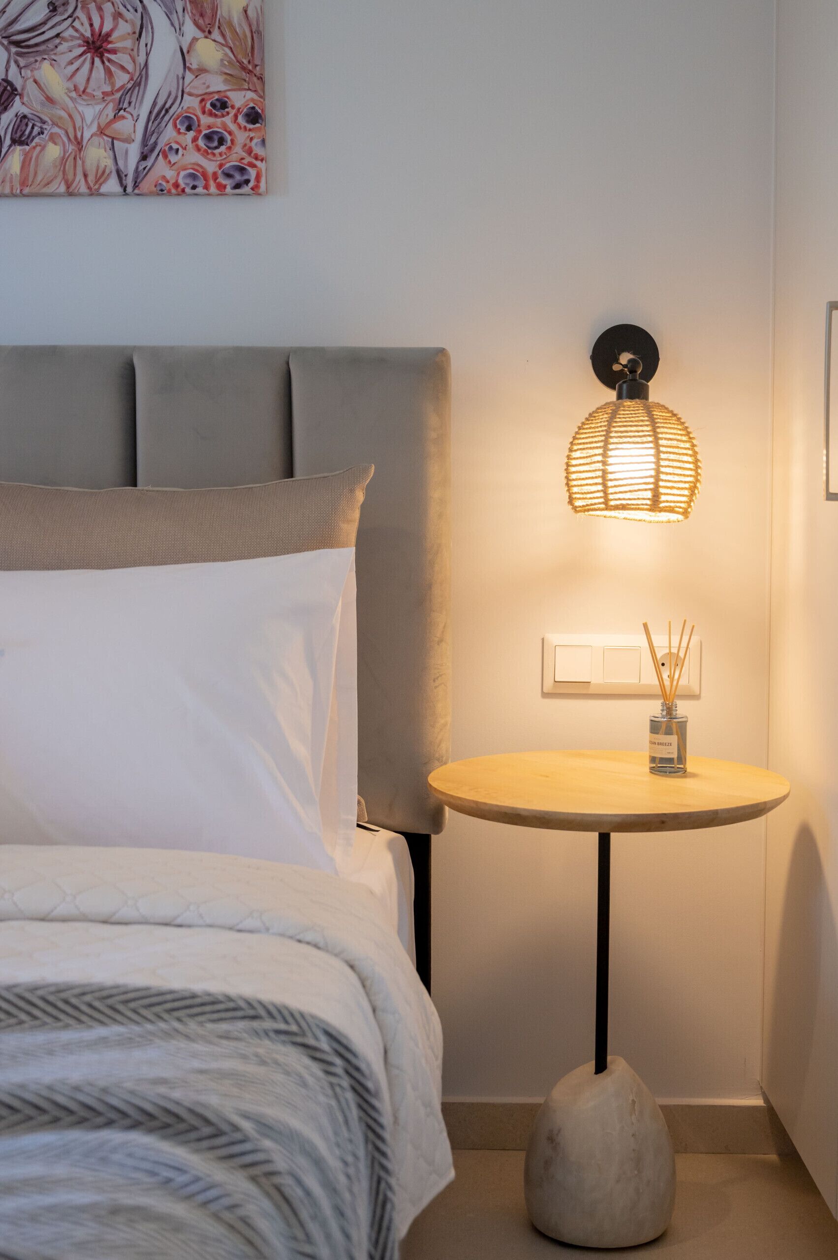 Una camera da letto con un letto, un comodino con una lampada e un punto luce a parete.