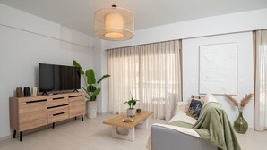 Un salon moderne avec un téléviseur, un meuble en bois, un canapé, une table basse et de grandes fenêtres avec des rideaux.