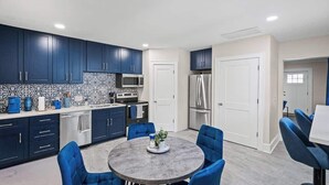 Una cocina moderna con armarios azul oscuro, una mesa redonda con sillas azules y un refrigerador.