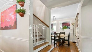 A staircase with a white railing, a dining area with a table and chairs, and a kitchen in the background. - Sleeps 10 - Plaza Midwood - Walk to Restaurants (Charlotte)