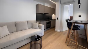 A modern kitchen with a built-in oven, a dining area with a table and chairs, and a living area with a sofa and a coffee table. - BlueMotion - CruiseNest Single  (Piraeus)